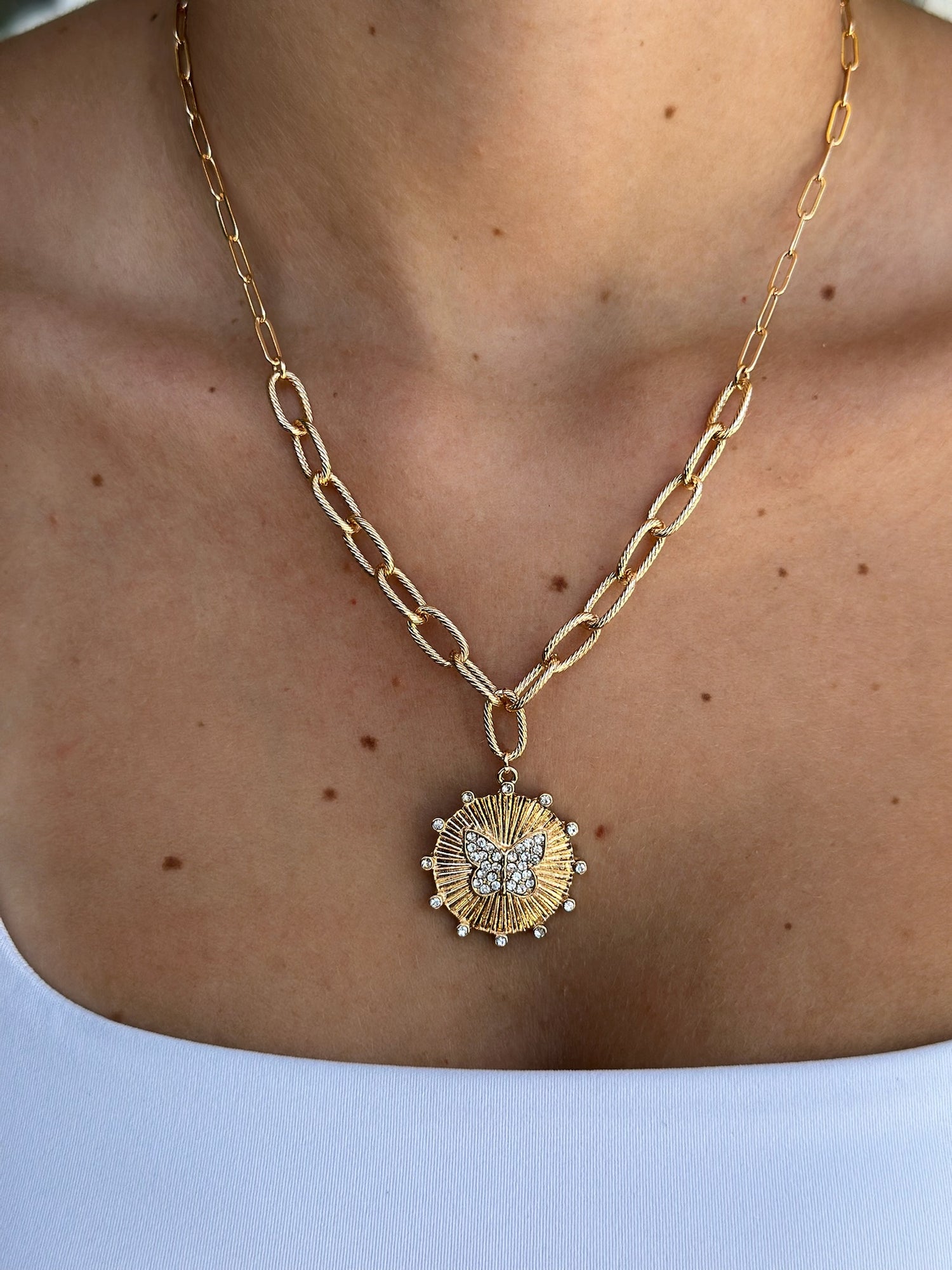 Gold chain necklace with a sunflower pendant on a person against a light background