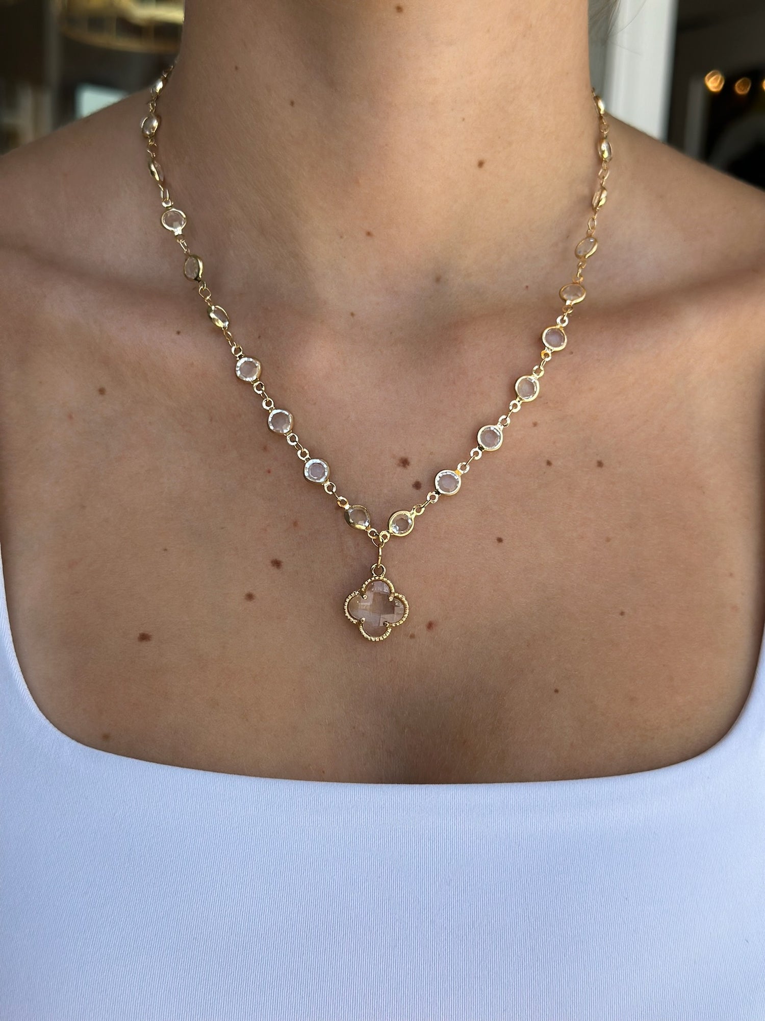 Gold necklace with a clover pendant on a person wearing a white top.