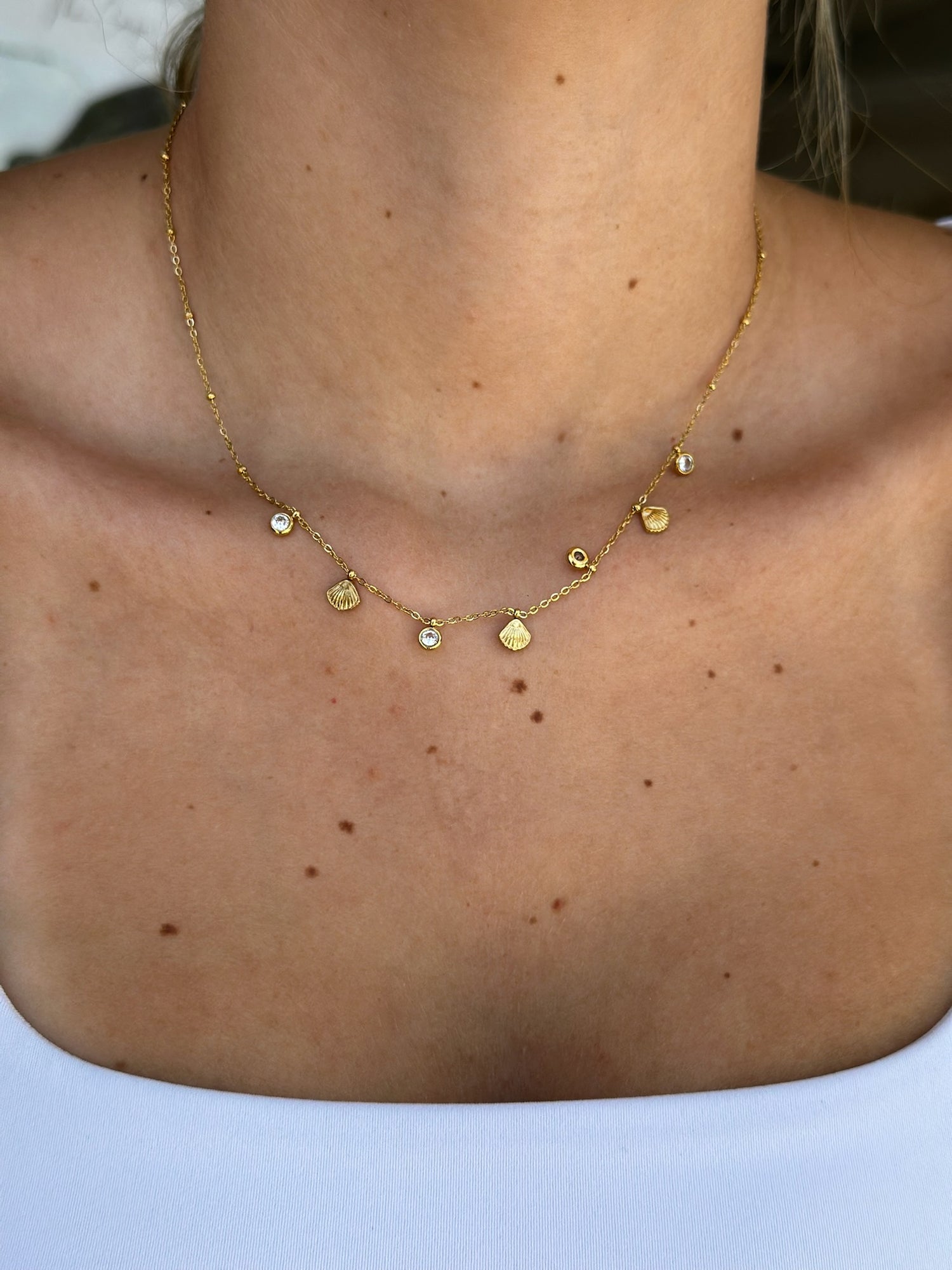 Gold necklace with small pendants on a person's neck against a neutral background