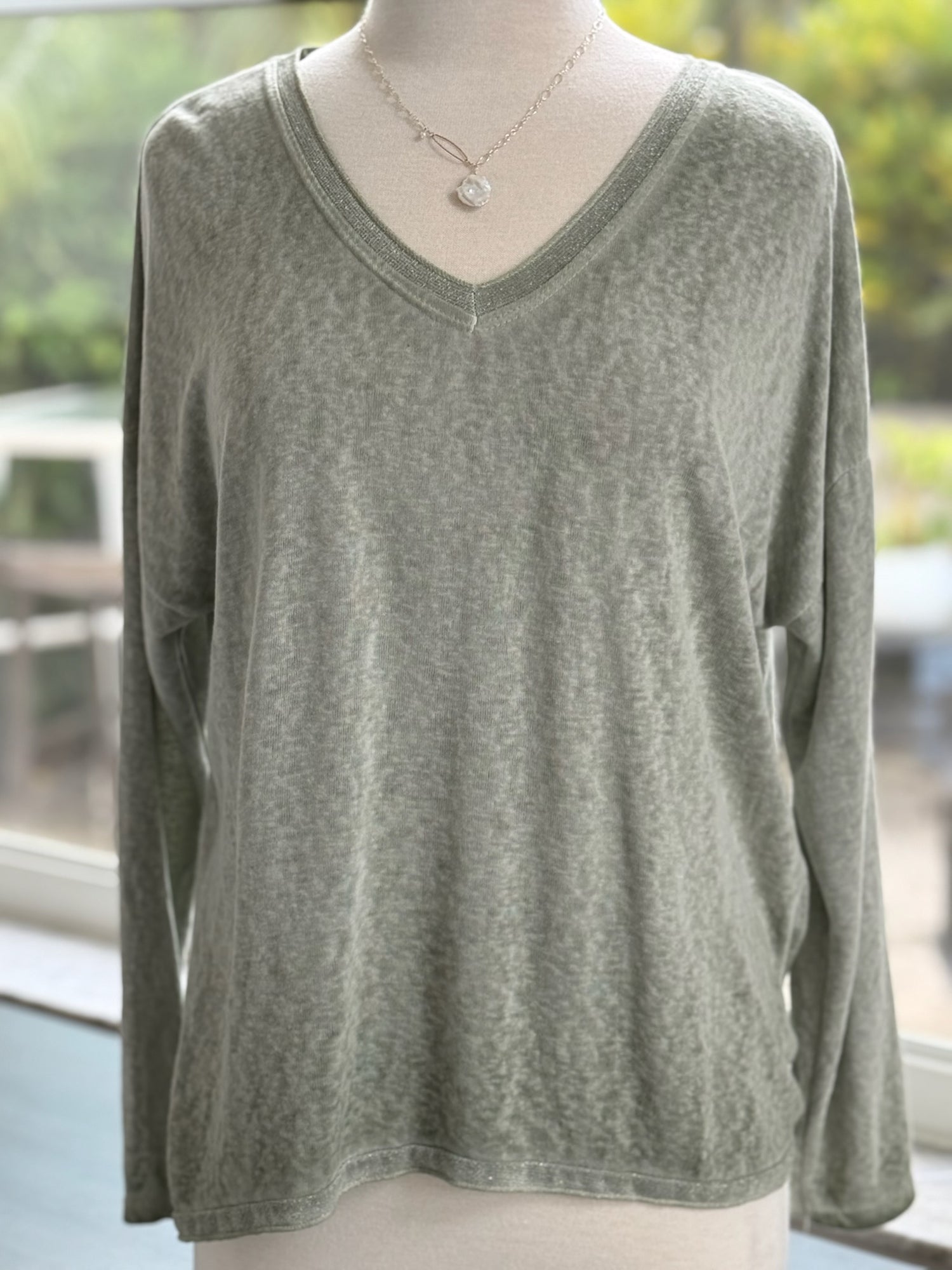 Soft sage green long-sleeve V-neck top with a relaxed fit, displayed on a mannequin indoors.
