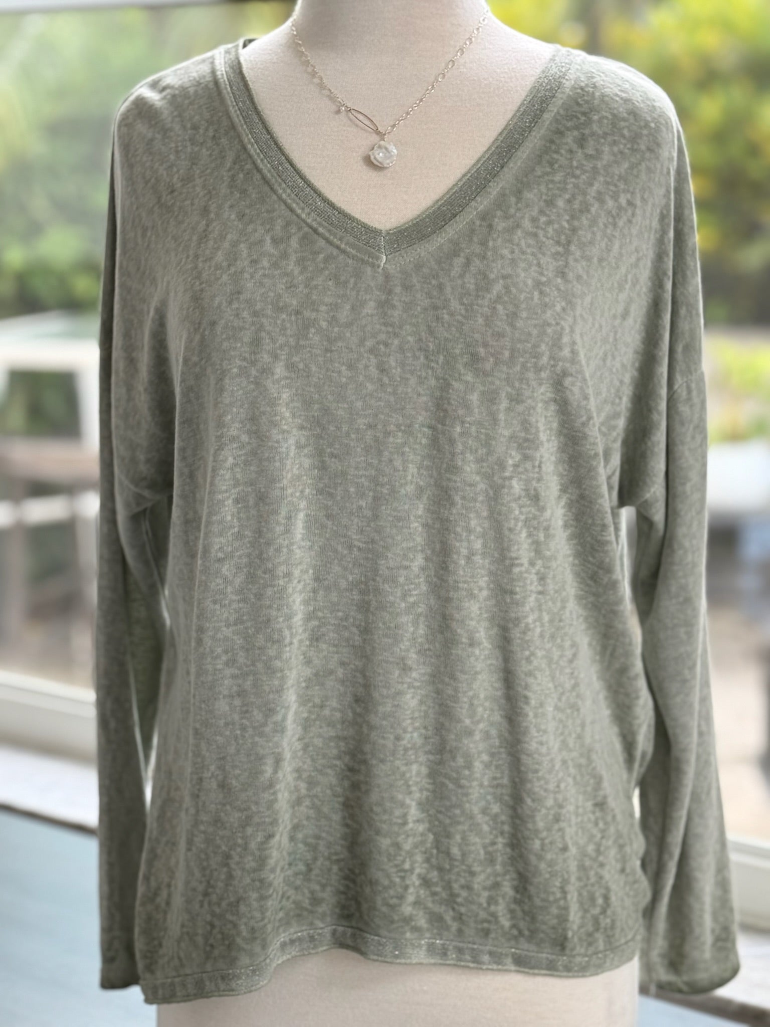 Soft sage green long-sleeve V-neck top with a relaxed fit, displayed on a mannequin indoors.