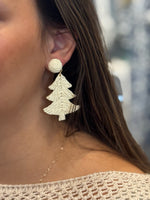 Close-up of a person wearing white Christmas tree earrings with a blurred background