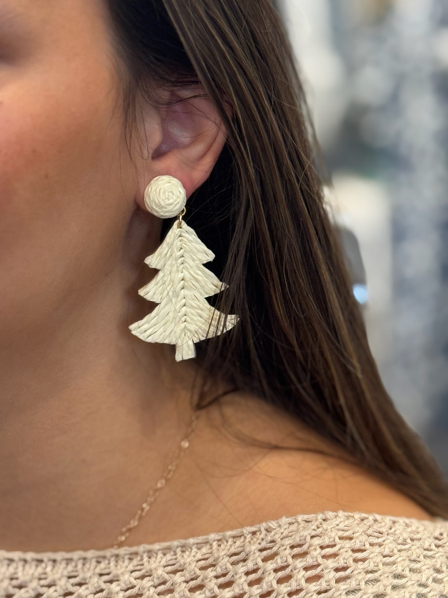 Close-up of a person wearing white Christmas tree earrings with a blurred background