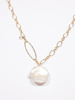 Handcrafted gold necklace featuring a large white Keshi freshwater pearl pendant on an elongated gold-filled link chain with a hammered oval accent and small pearl charm. Elegant and asymmetrical design from the Nina Halls collection.