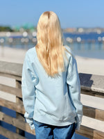 Person wearing a light blue sweatshirt by a waterfront on a sunny day