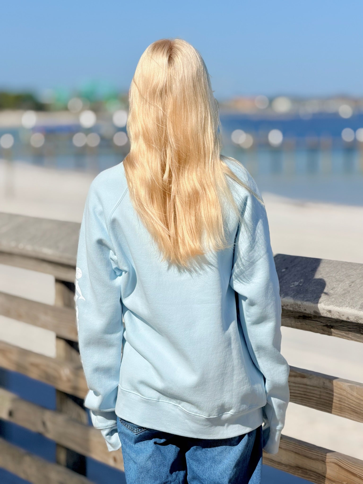 Person wearing a light blue sweatshirt by a waterfront on a sunny day