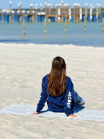 Person sitting on a towel at the beach with a dock in the background