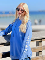 Woman wearing a periwinkle blue hoodie with a beach background