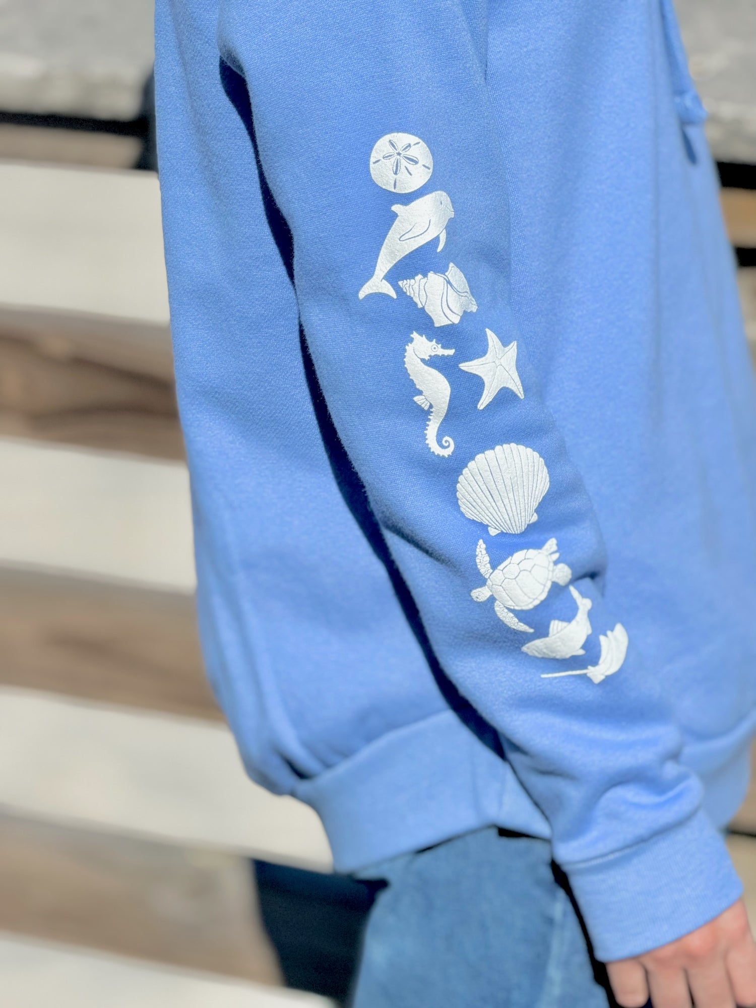 Close-up of white sea life icons printed along sleeve of periwinkle women’s coastal hoodie