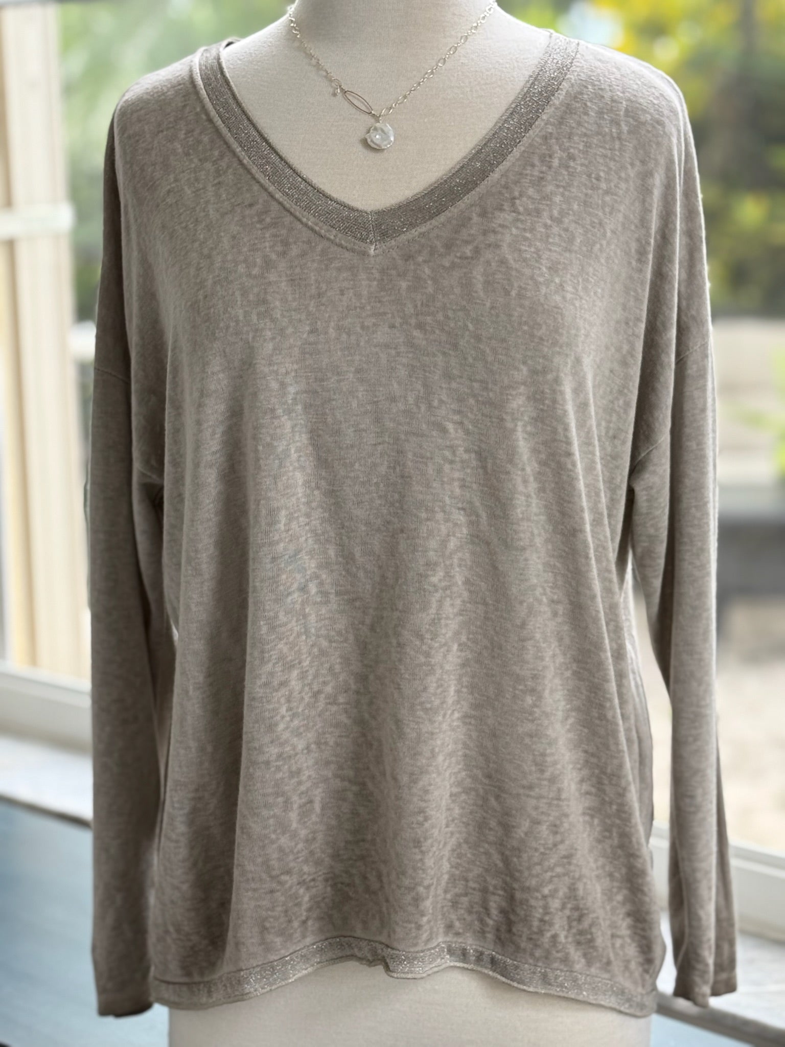 A lightweight taupe-colored sweater with silver trim on the neckline and bottom hem, displayed on a mannequin.