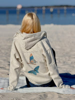 Person wearing a hoodie with butterfly designs sitting on a beach.