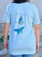 Sea Mist t-shirt with butterfly design and text "Then Sings My Soul" worn by a person outdoors.