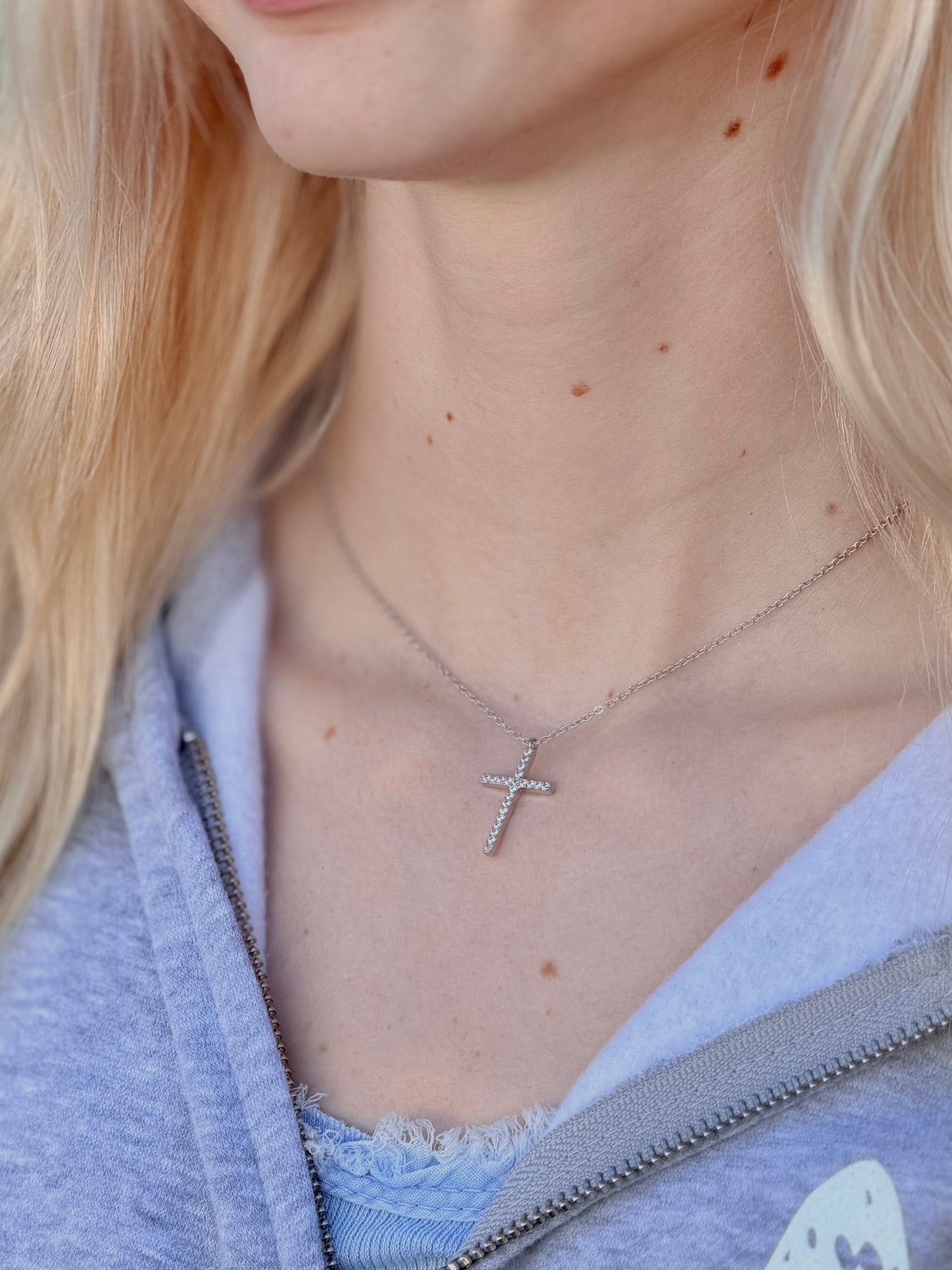Person wearing a silver sparkly cross necklace 