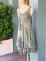 Sleeveless olive dress with navy palm print and a flowy layered hem, displayed on a mannequin.