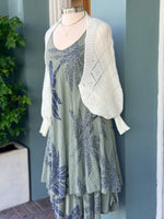 Sleeveless olive palm print dress in navy tones layered with a white open-knit cardigan, displayed on a mannequin.