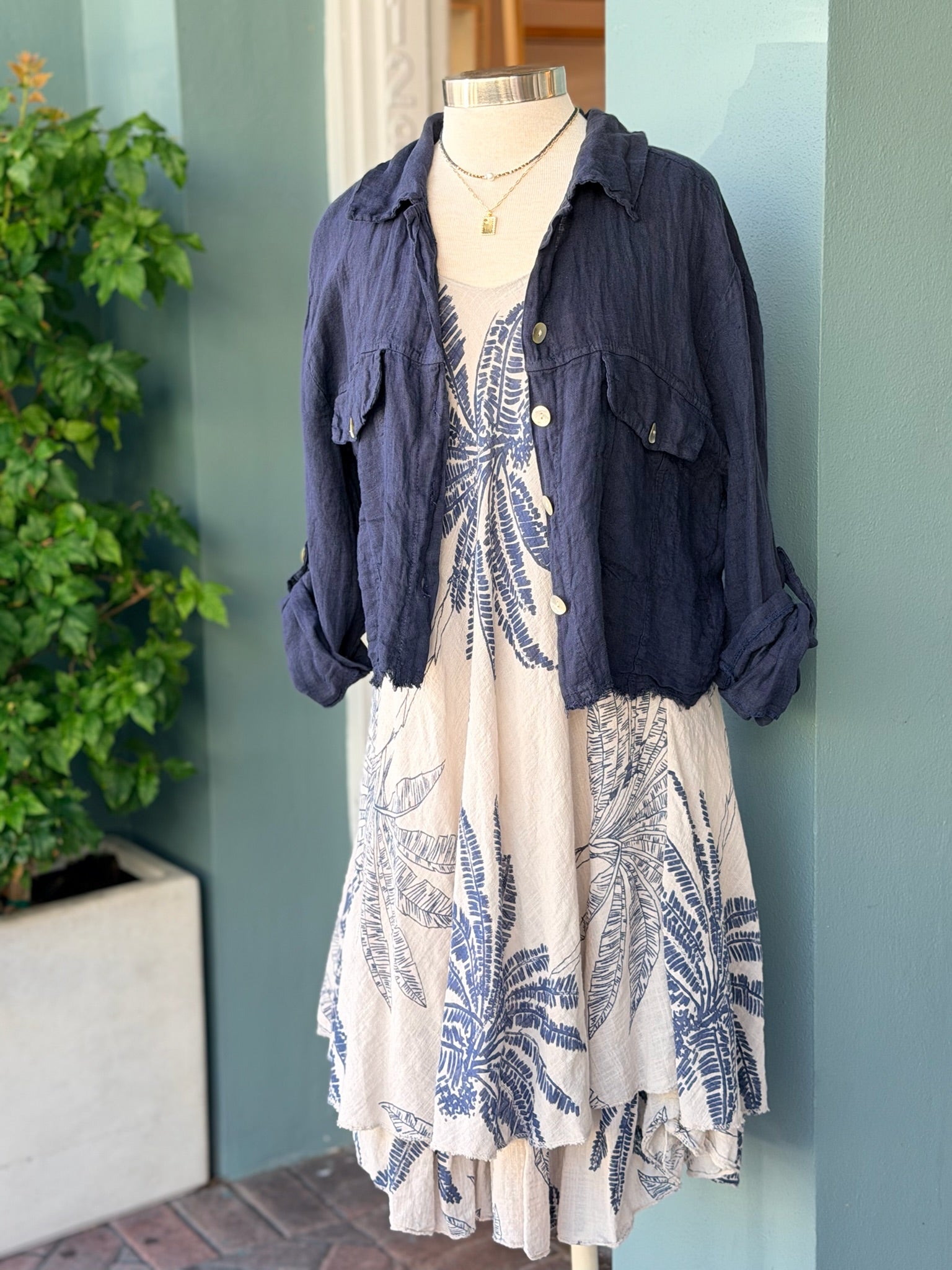 Lightweight sleeveless dress in taupe with navy palm leaf pattern and layered hem, styled on a mannequin.
