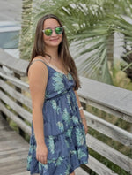 Model wearing a short blue dress with aqua floral print, styled with gold jewelry and sunglasses side view