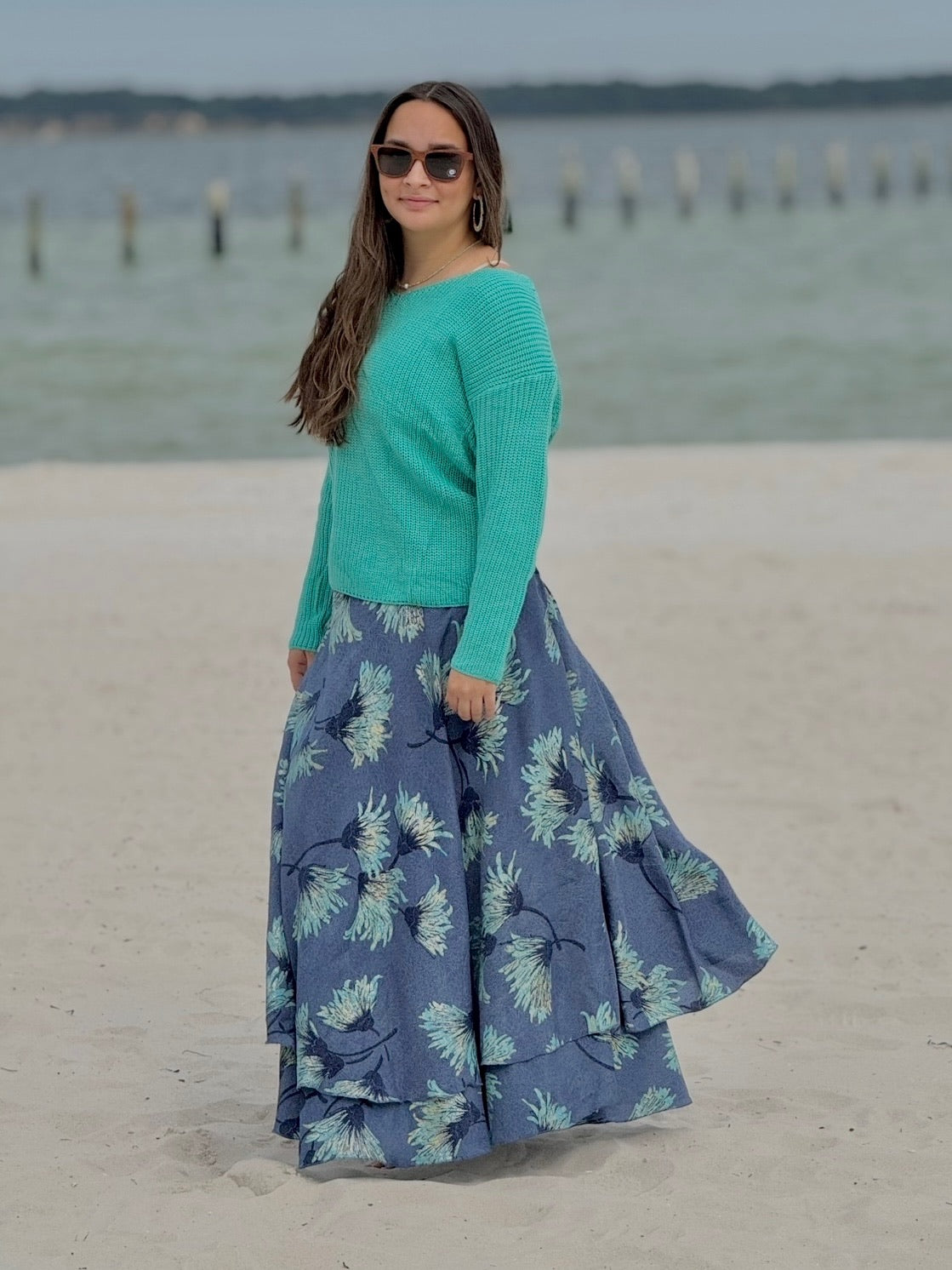 Model wearing layered skirt with a soft aqua base with blue floral print, paired with an aqua sweater