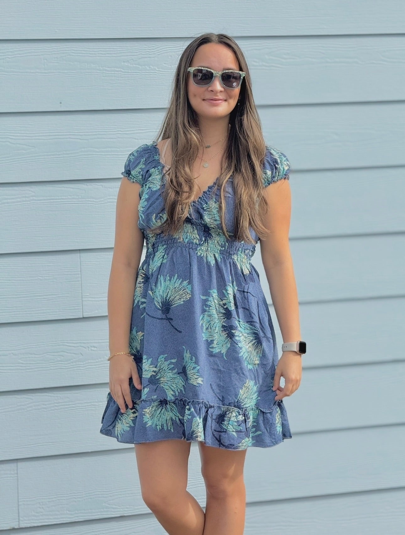 Woman wearing a blue floral dress standing against a light blue wall.