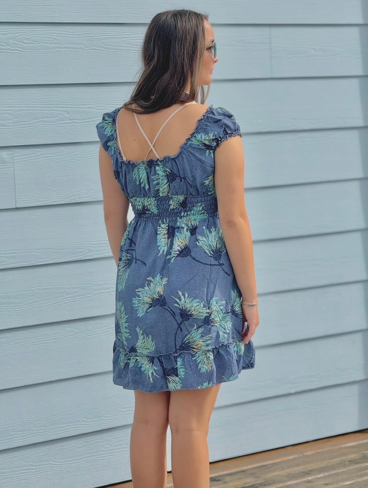 Woman wearing a blue floral dress standing against a light gray wall.