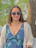 Woman wearing sunglasses and a floral dress with a beige cardigan outdoors.