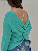 Person wearing a turquoise knitted top with a floral patterned skirt on a plain background