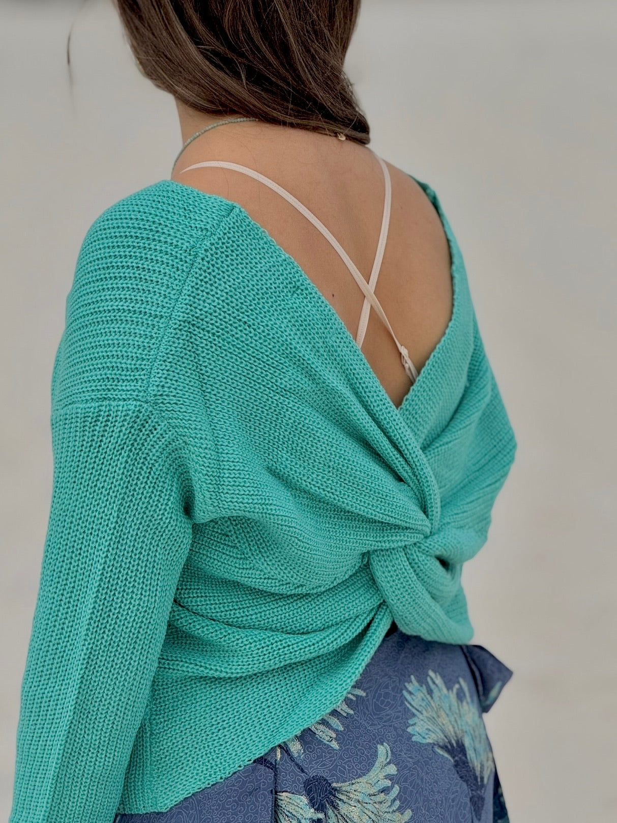 Person wearing a turquoise knitted top with a floral patterned skirt on a plain background