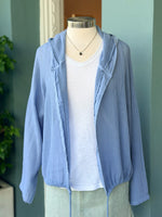 Mannequin wearing a light blue cardigan over a white shirt against a green wall.