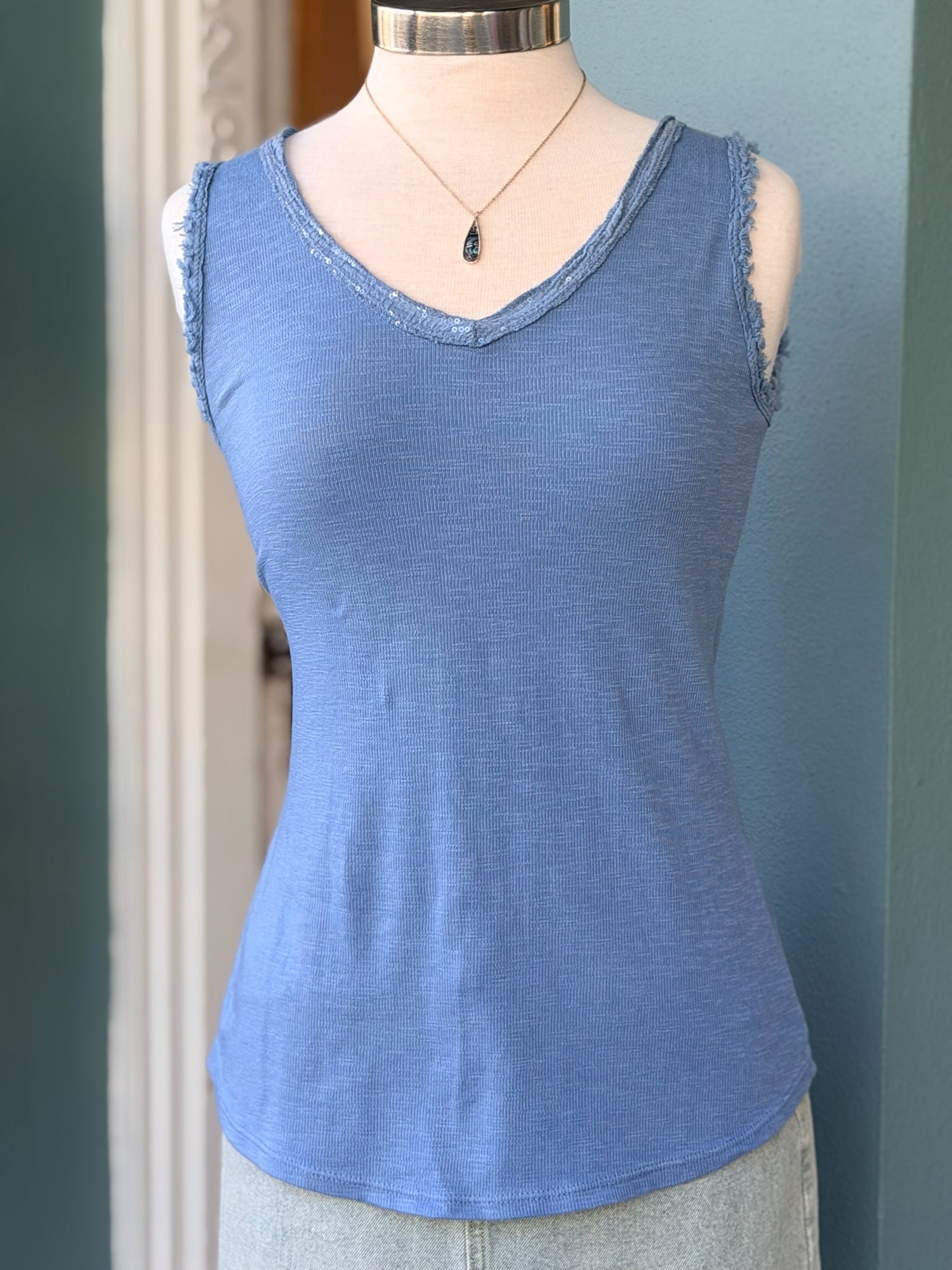Blue sleeveless tank top with subtle sequin-trimmed V-neckline on a mannequin