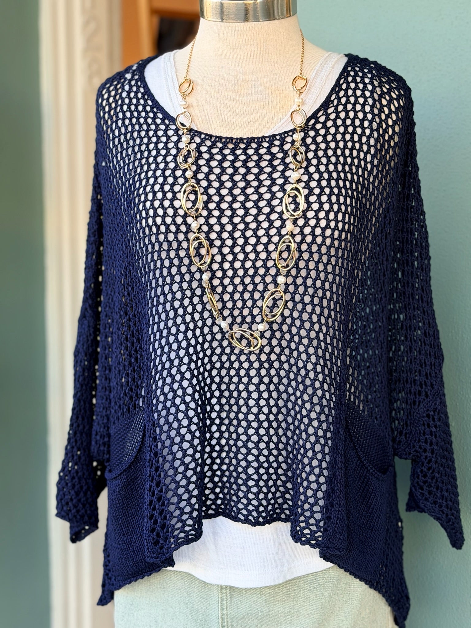 Navy blue knit cardigan on a mannequin with gold necklace against a green wall.