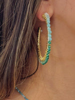 Close-up of a person wearing a colorful beaded earring with gold and green tones.