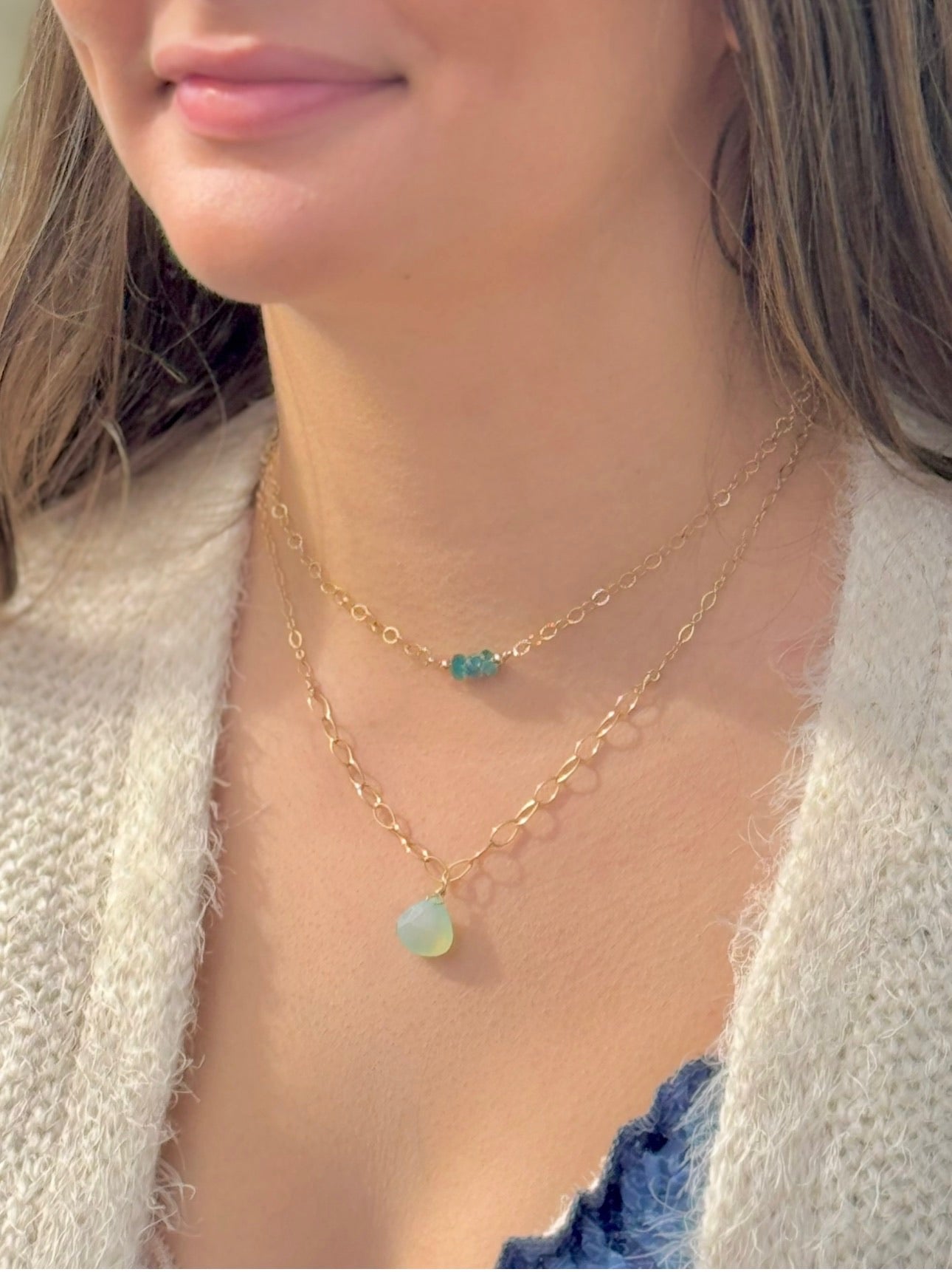 Close-up of a person wearing two gold necklaces with gemstone pendants.