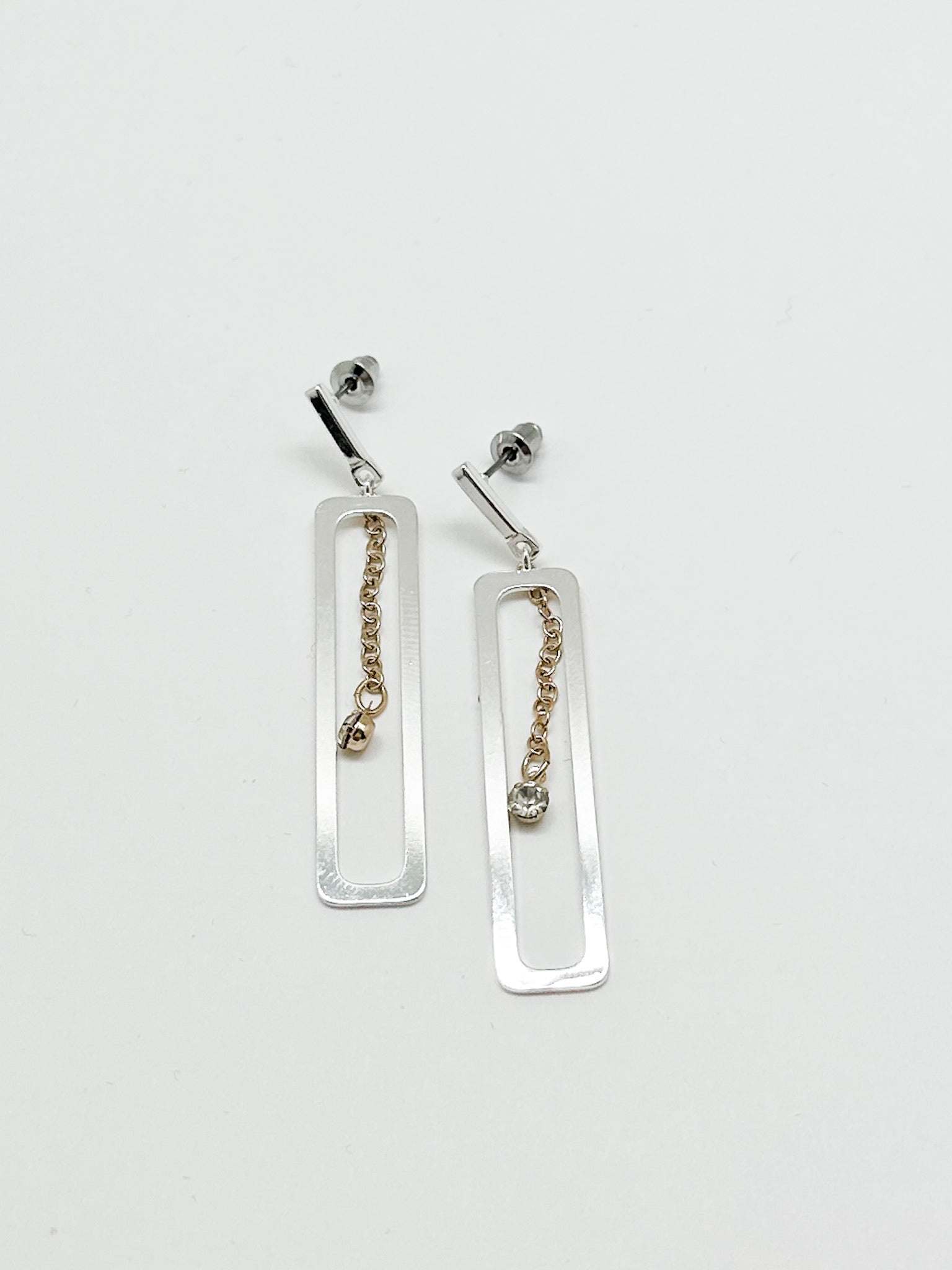 Shelby earring. silver dangly rectangle with a gold chain with tiny crystal in center. 
