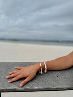 "Camille cloisonné bracelet worn at the beach – subtle dove grey enamel tones"
