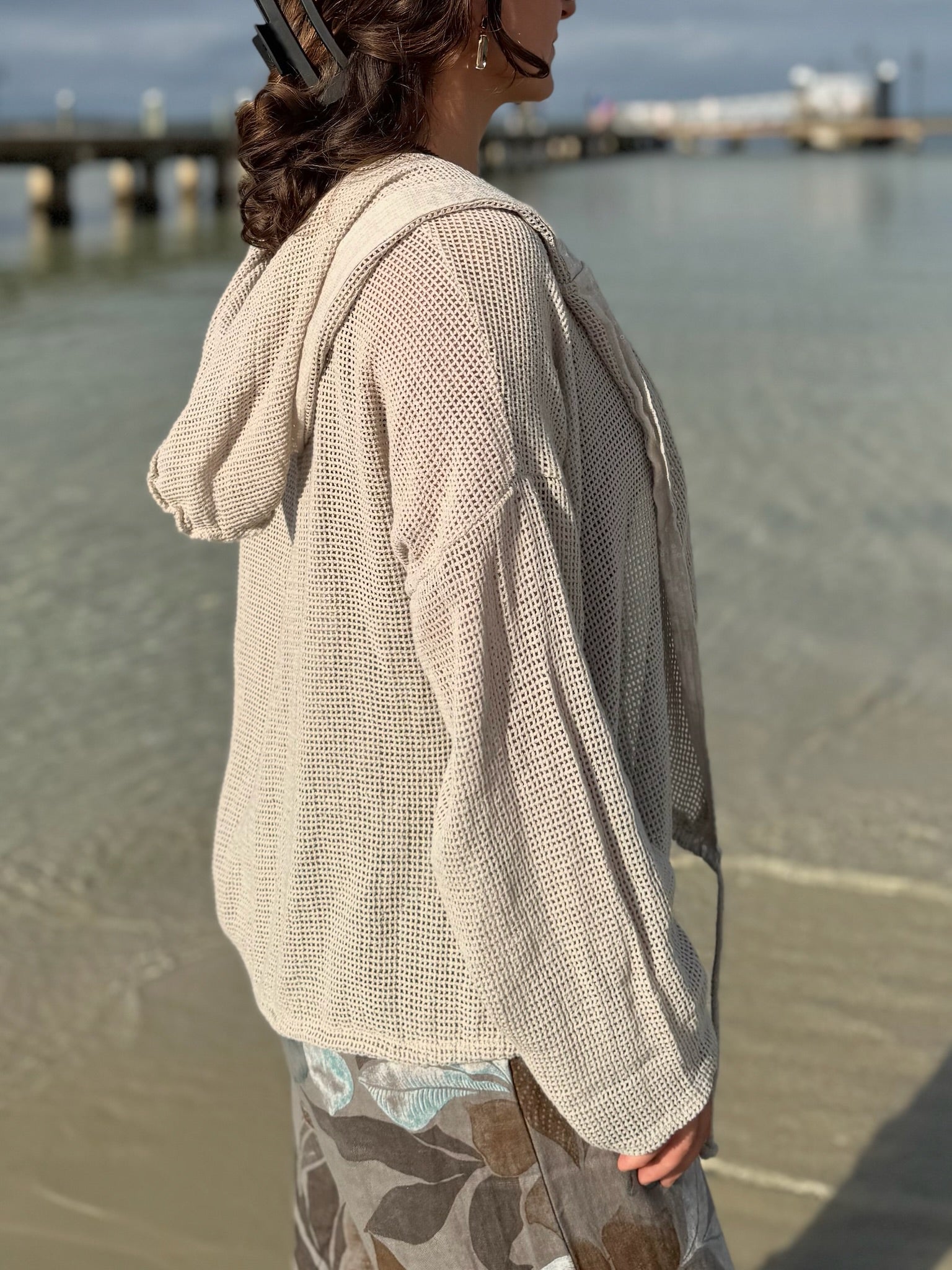 Side view of the beige Gia Mesh Hooded Jacket showing the open-knit texture, loose fit, and hood draped naturally down the back.