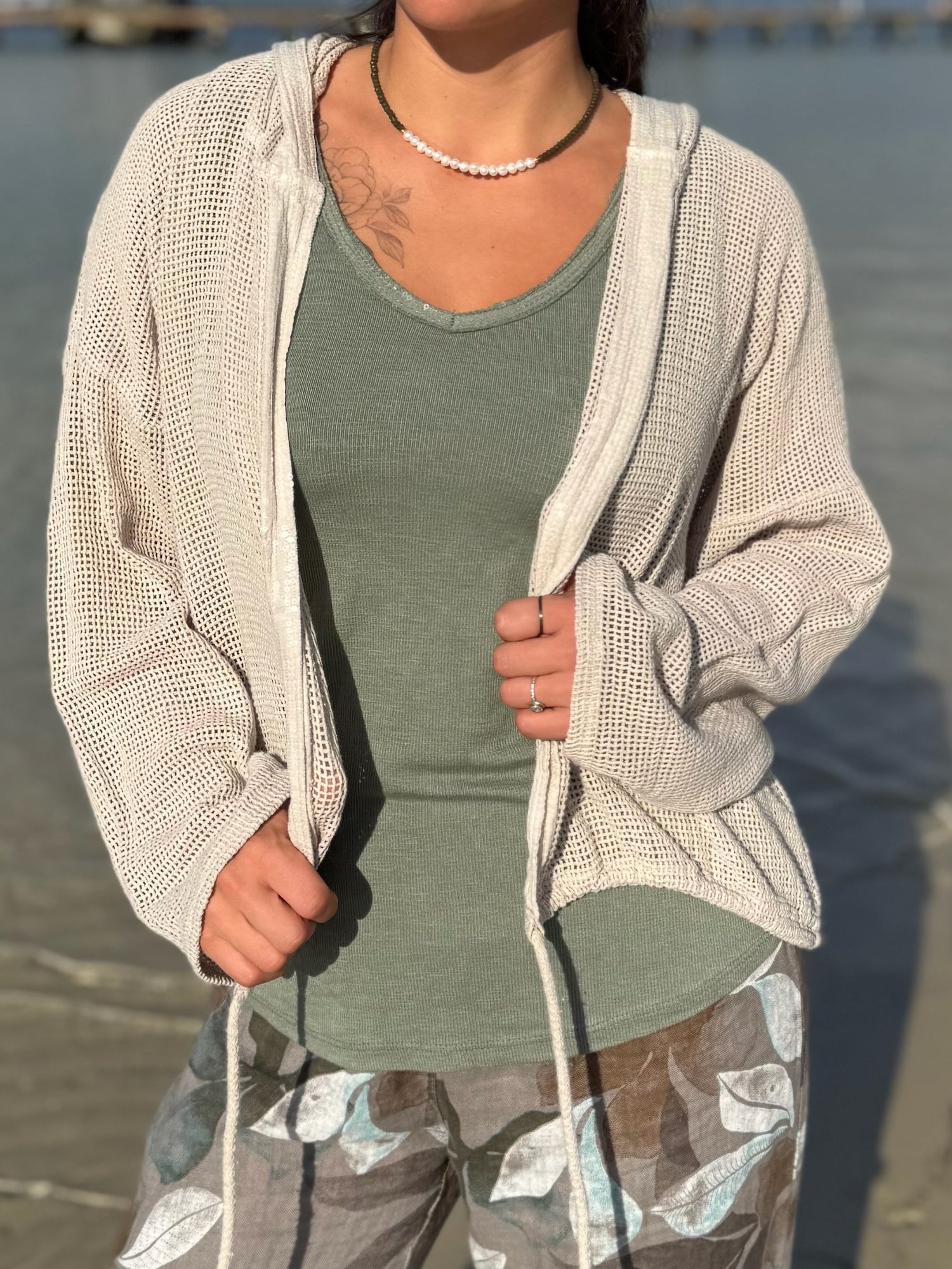 Close-up of the Gia Mesh Hooded Jacket in beige, worn over a sage green tank, highlighting the airy mesh knit and relaxed drape.