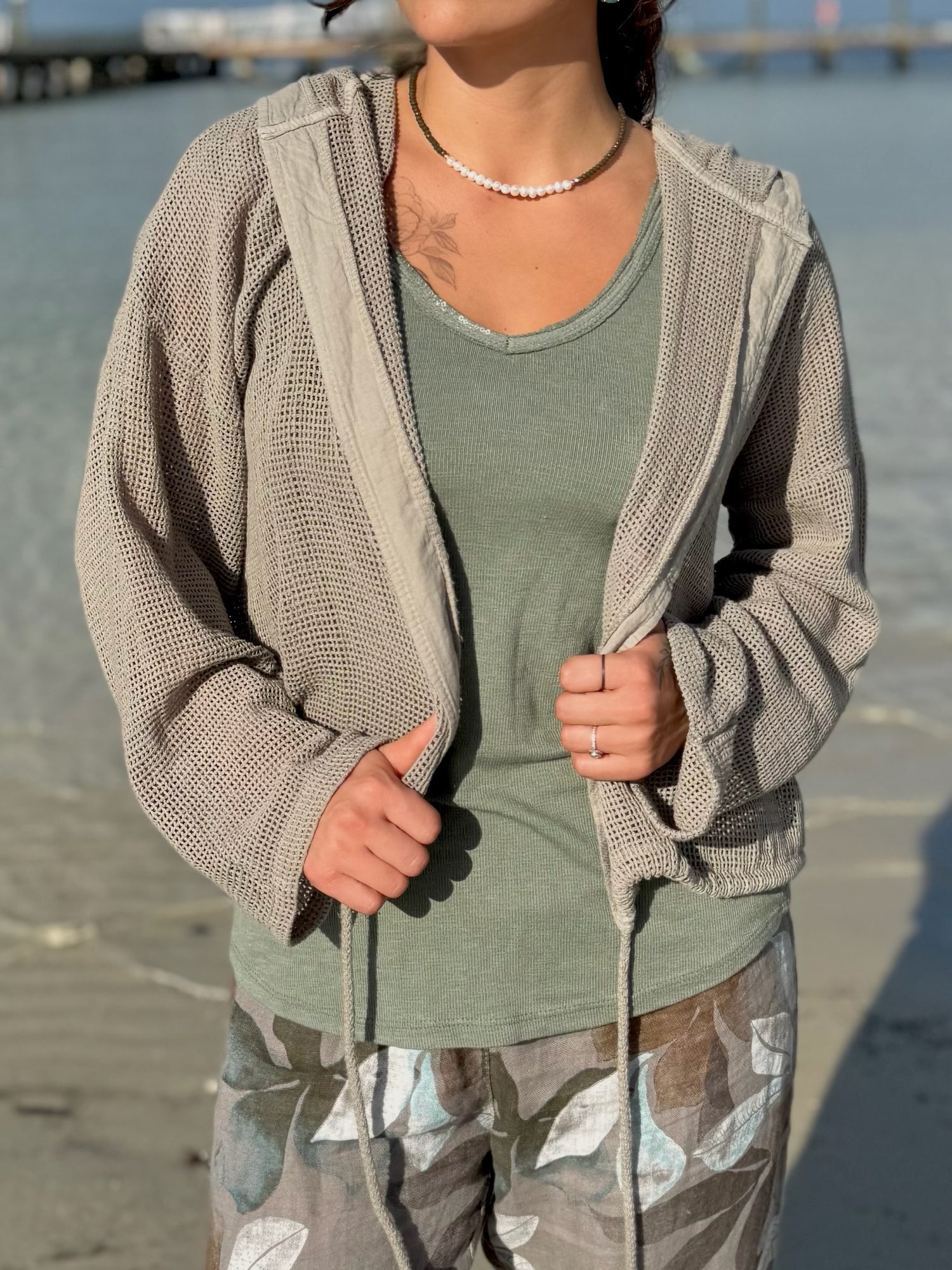 Close-up of the taupe Gia Mesh Hooded Jacket worn over a sage tank, showing the mesh texture, hood, and front zipper in warm sunlight.