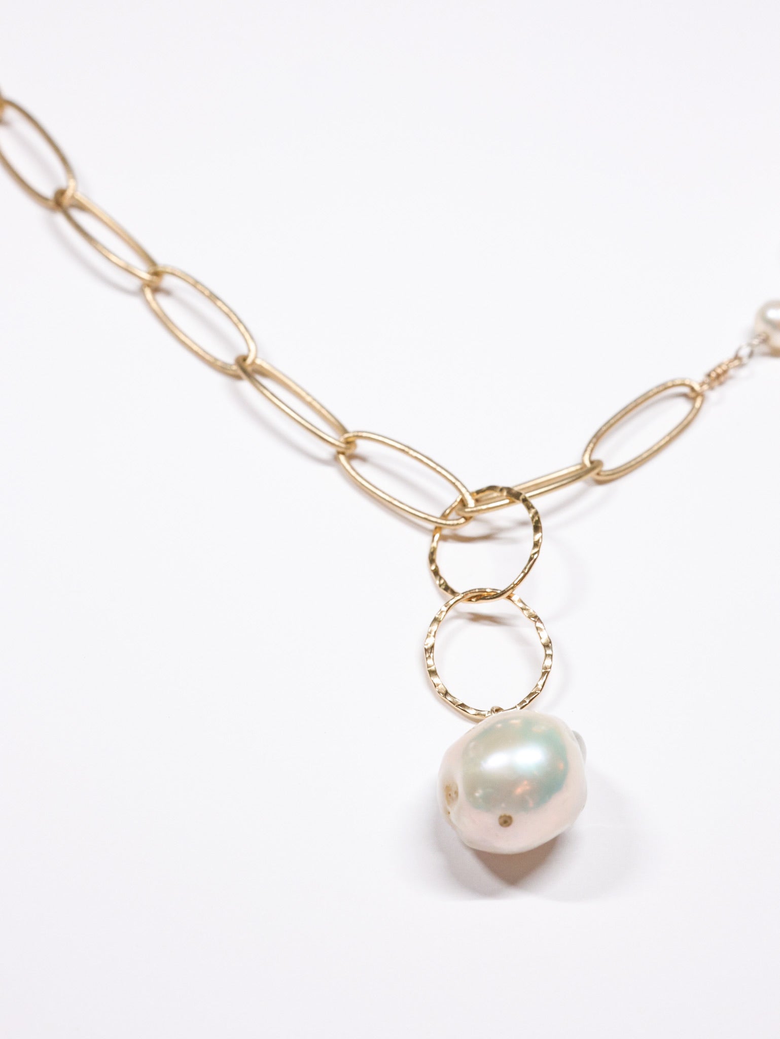 Close-up of the Grace Pearl NH Necklace from Ardor Boutique, featuring a matte gold link chain, hammered rings, and a large baroque freshwater pearl drop.
