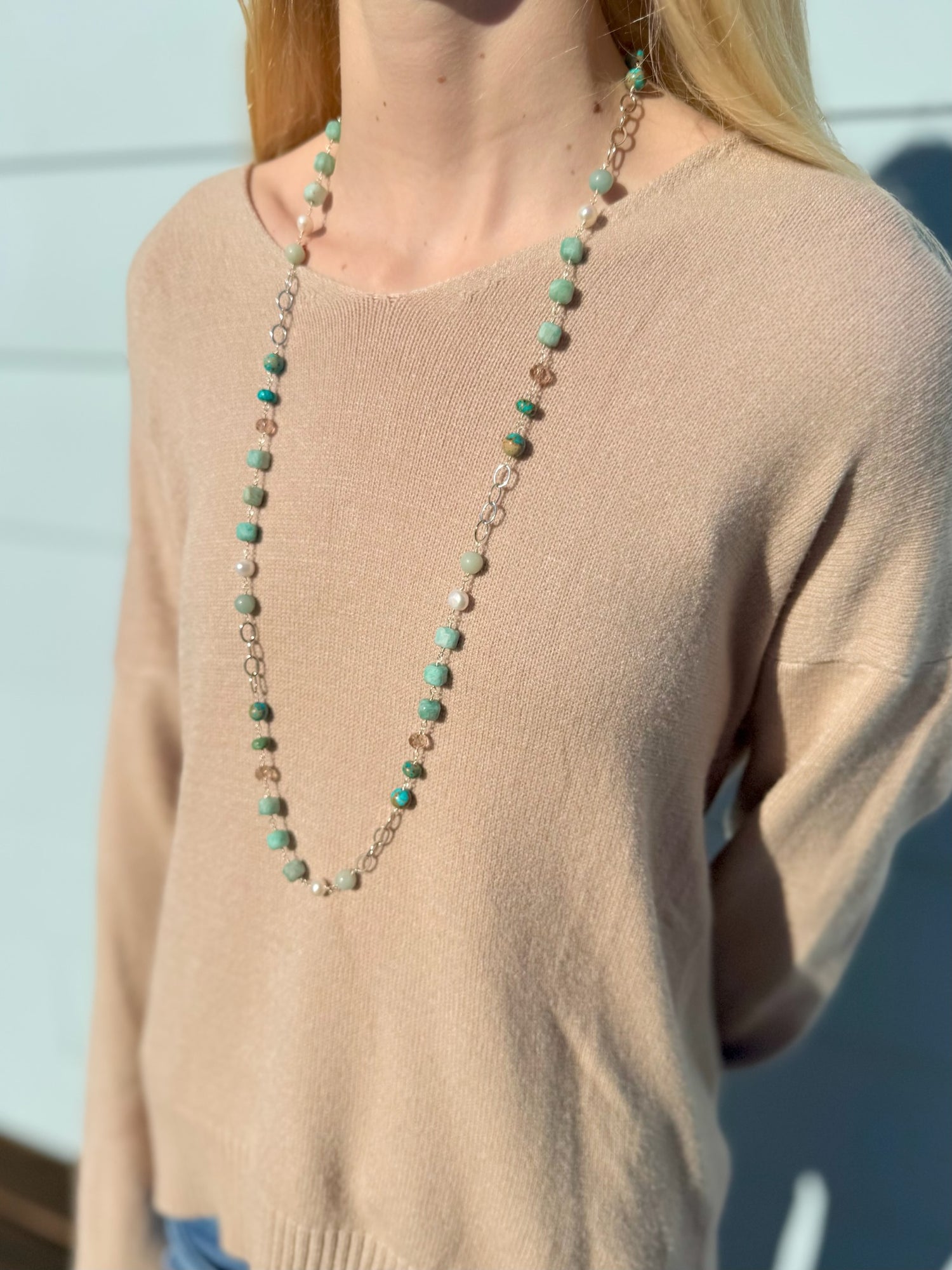 Person wearing a long beaded necklace with a neutral background