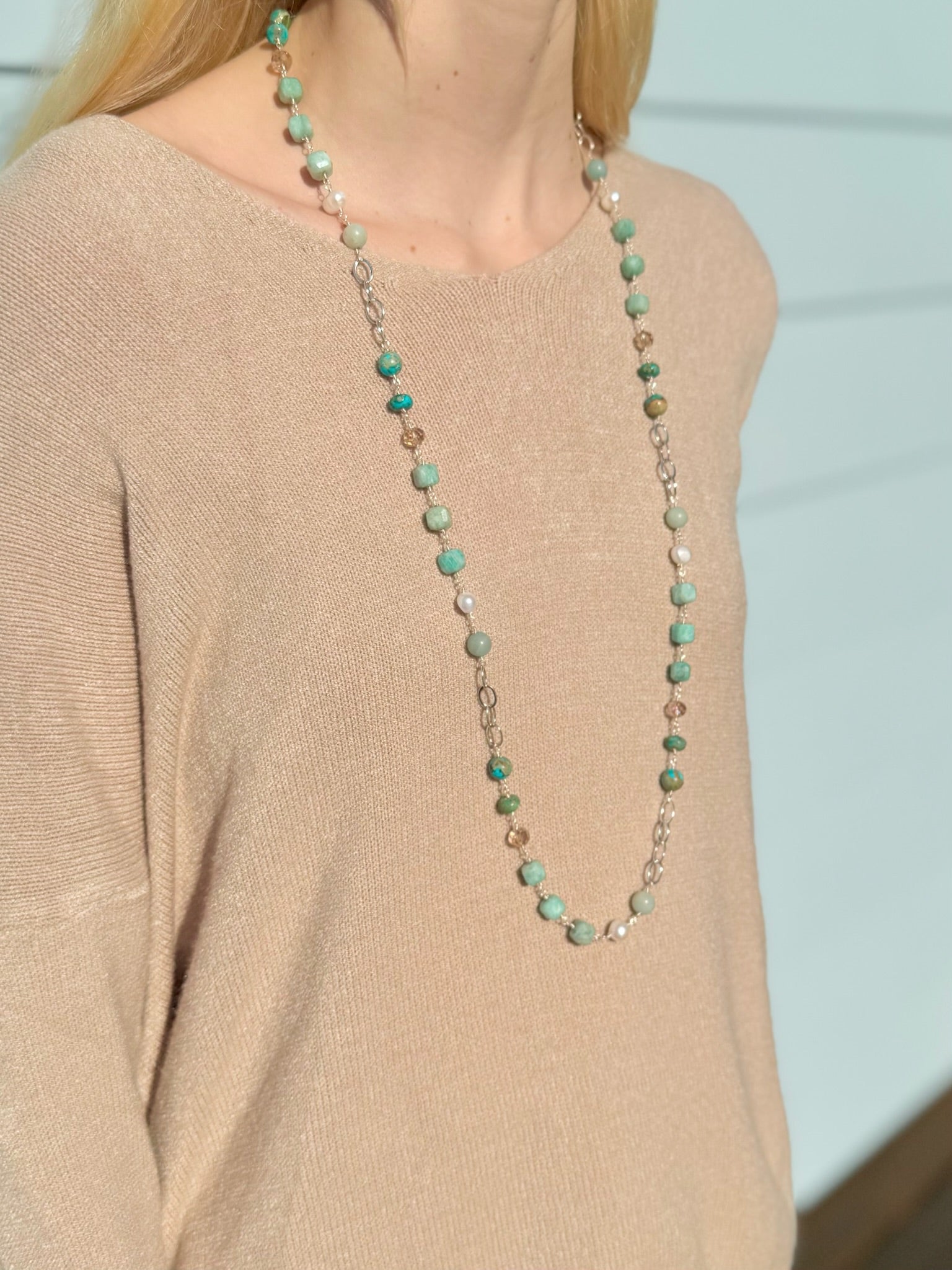 Long necklace with green beads worn by a person in a beige sweater.