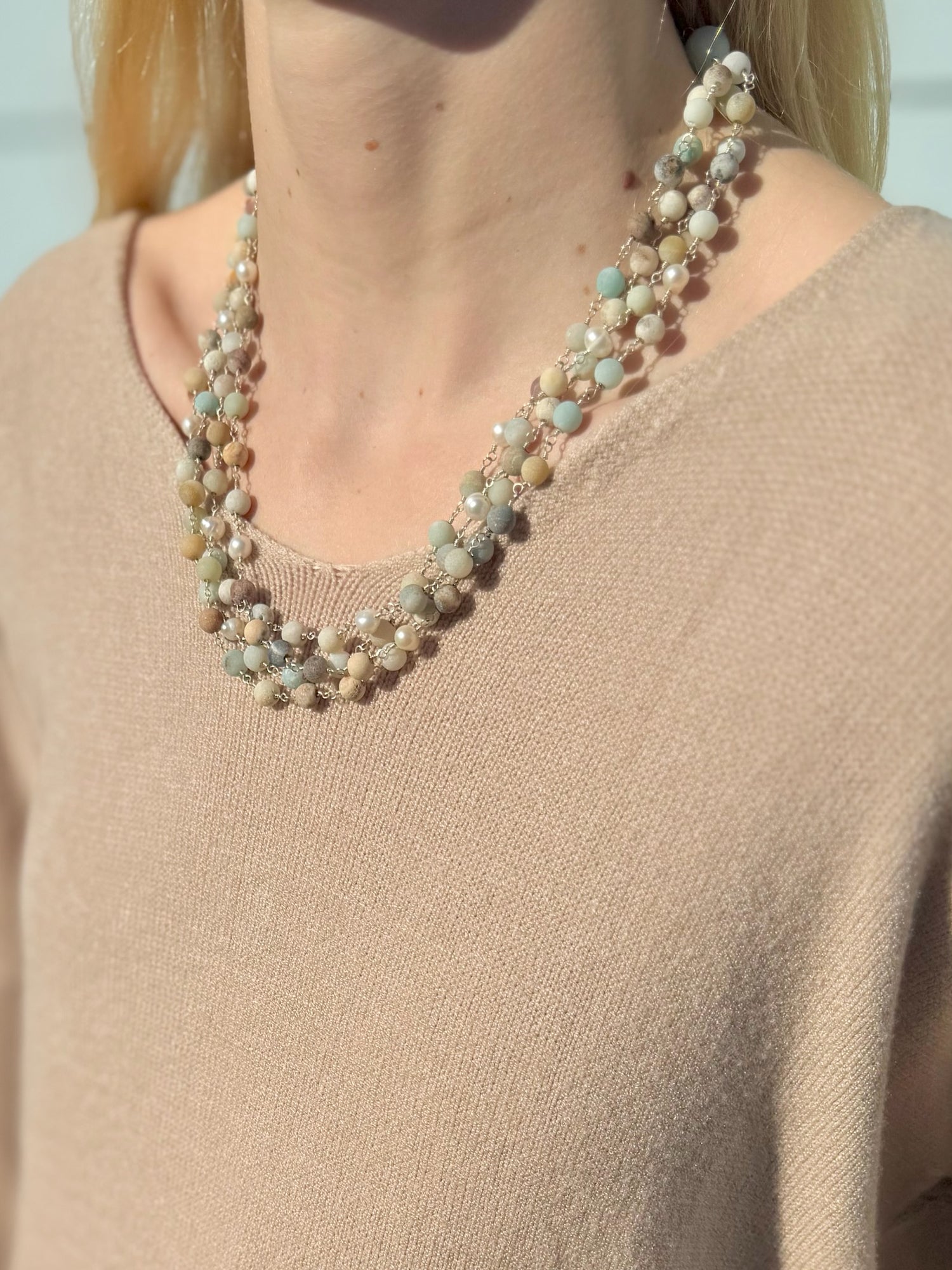 Necklace with multicolored beads worn by a person in a beige sweater.
