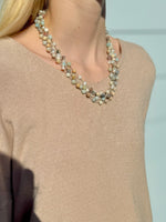 Necklace with multicolored beads worn by a person in a beige sweater against a light blue background