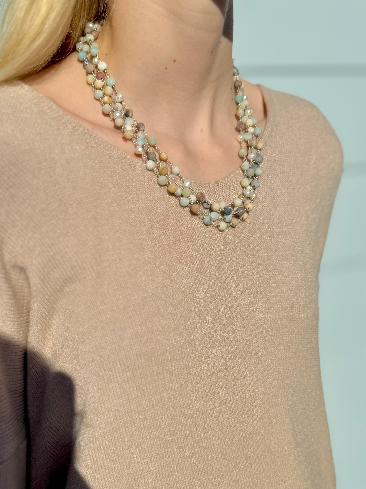 Necklace with multicolored beads worn by a person in a beige sweater against a light blue background