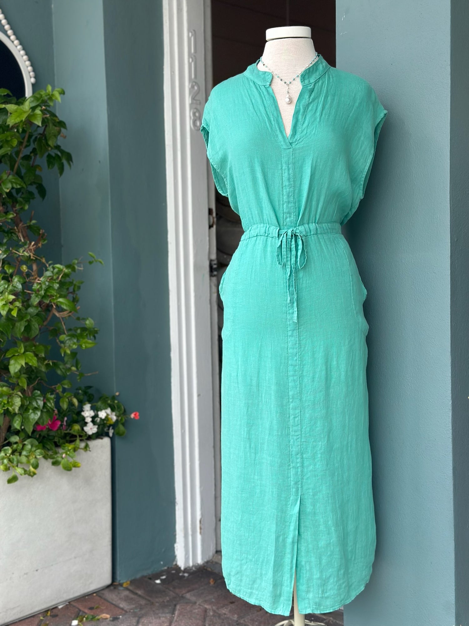 
Sharon Dress in turquoise teal linen with adjustable drawstring waist, split neckline, cap sleeves, midi length, and side pockets, made in Italy.