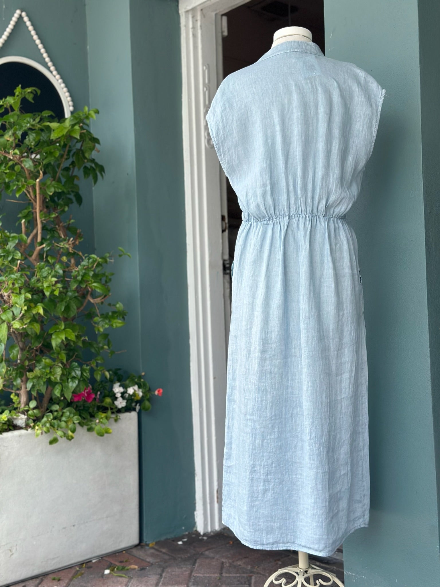 Back view of a sky blue linen midi dress featuring cap sleeves, an elasticized waist detail, and an easy, flowing silhouette in breathable linen.