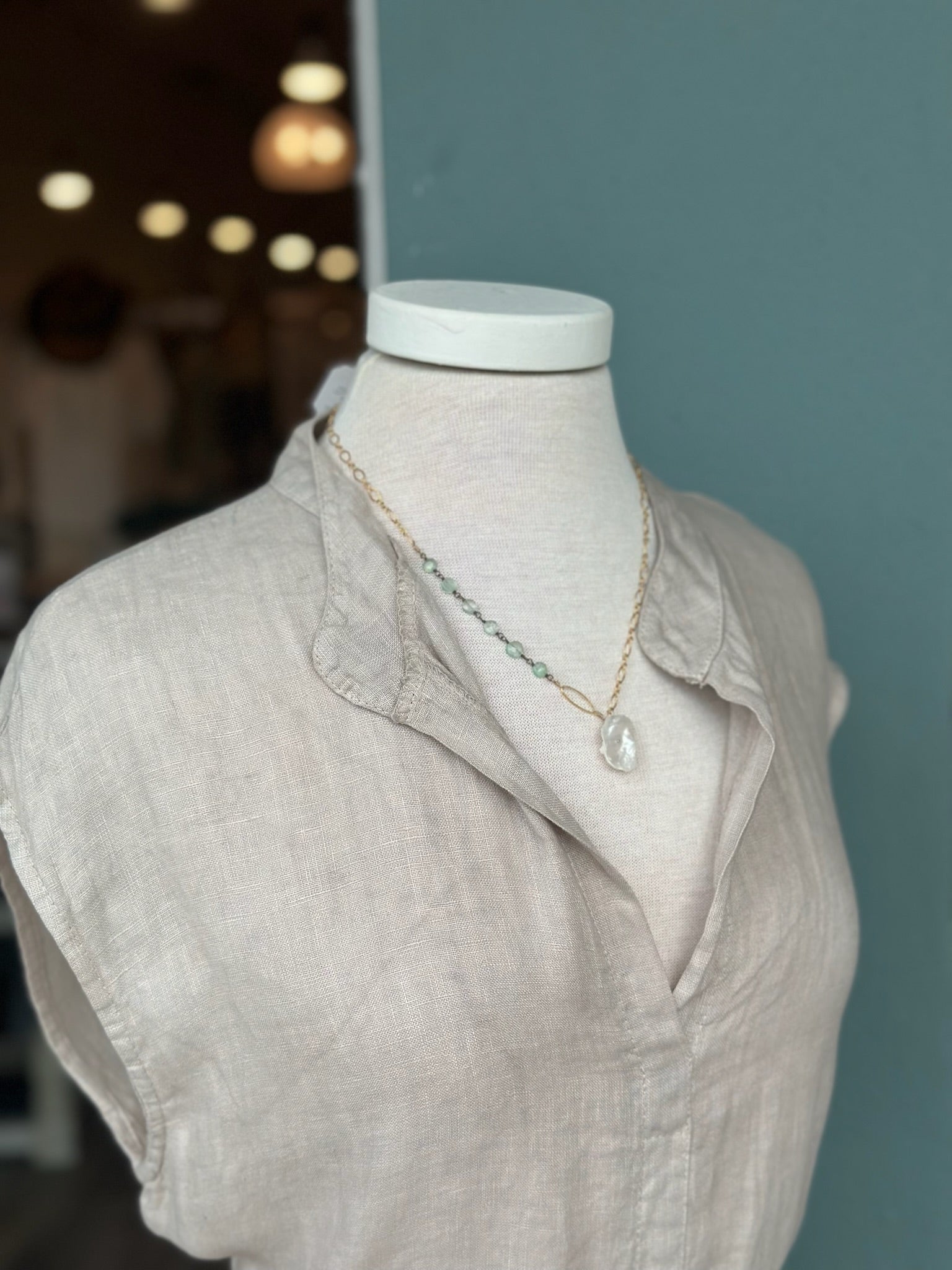 Green gemstone and freshwater pearl pendant necklace styled with the Sharon Linen Dress in Oatmeal Beige, featuring a delicate gold chain and organic pearl accent against a soft Italian linen split neckline.
