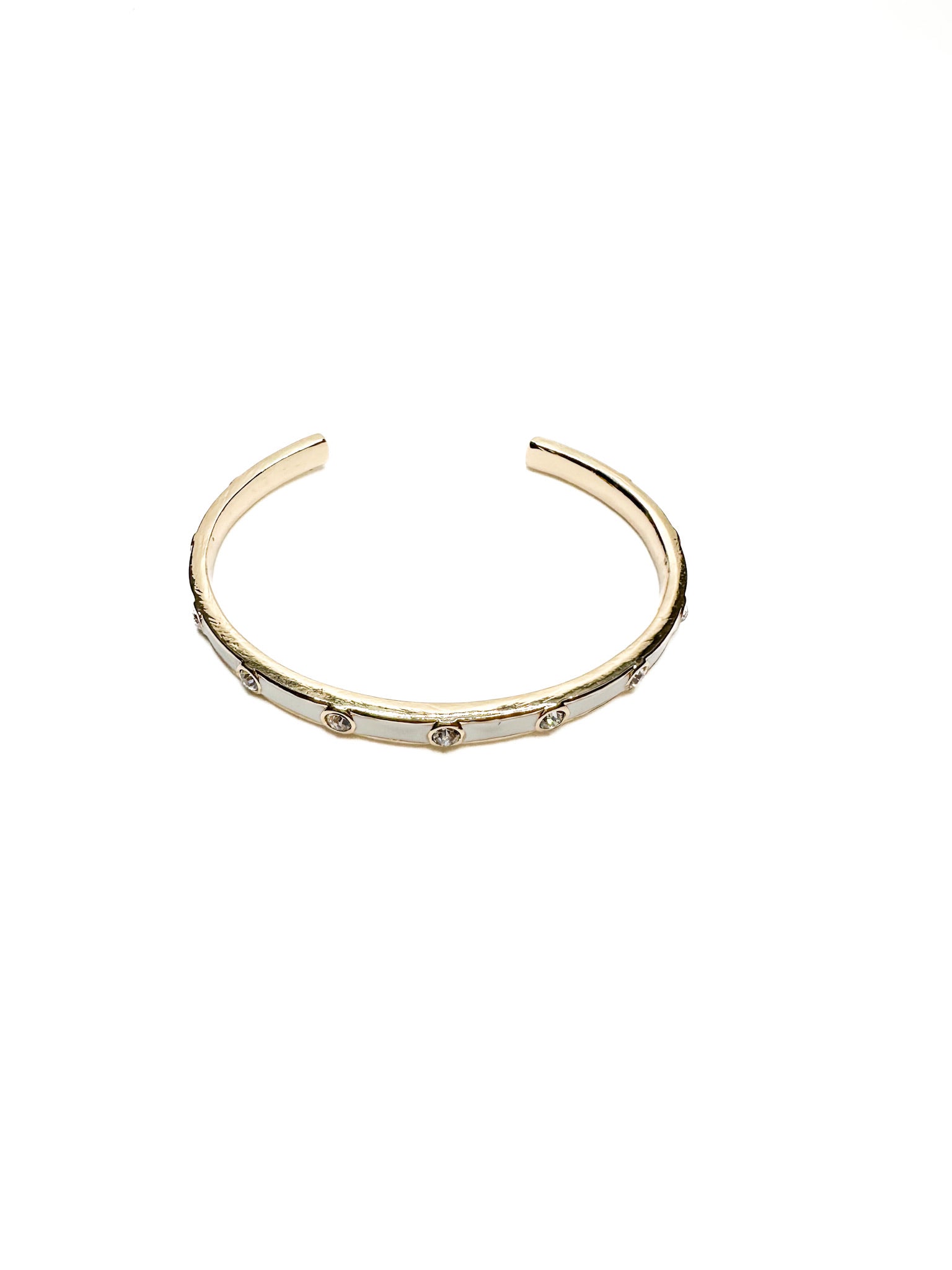 Gold open cuff bracelet with white enamel inlay and clear crystal accents, displayed on a white background.
