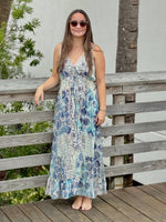 Woman in a floral dress standing on a wooden deck with a wooden fence and greenery in the background.