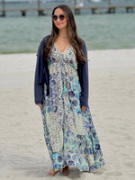 Woman in a floral dress and navy cardigan standing on a beach.