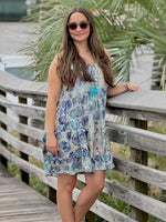Woman in a floral dress standing on a wooden deck with greenery in the background